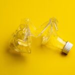 A crushed plastic bottle on a yellow background showcasing plastic waste management importance